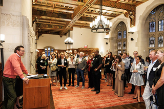Attendees standing together listening to Gunnar S Overstrom, Chair of Parents Leadership Council, speaking at a podium during the 2024 PLC Fall Gathering